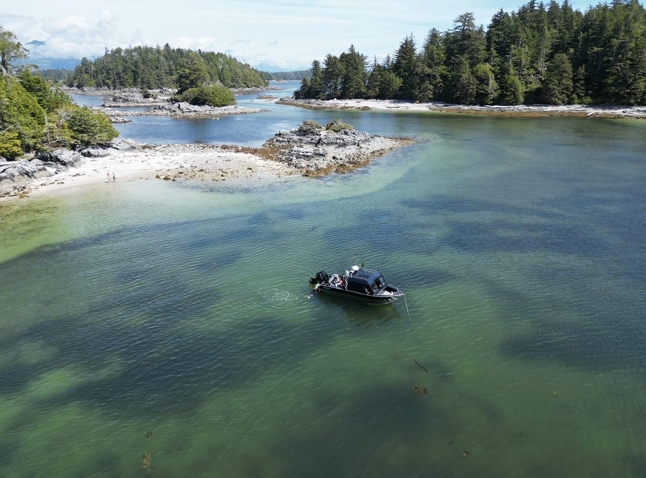 Aerial view of a small boat anchored in a green-blue cove between rocky islets and forest