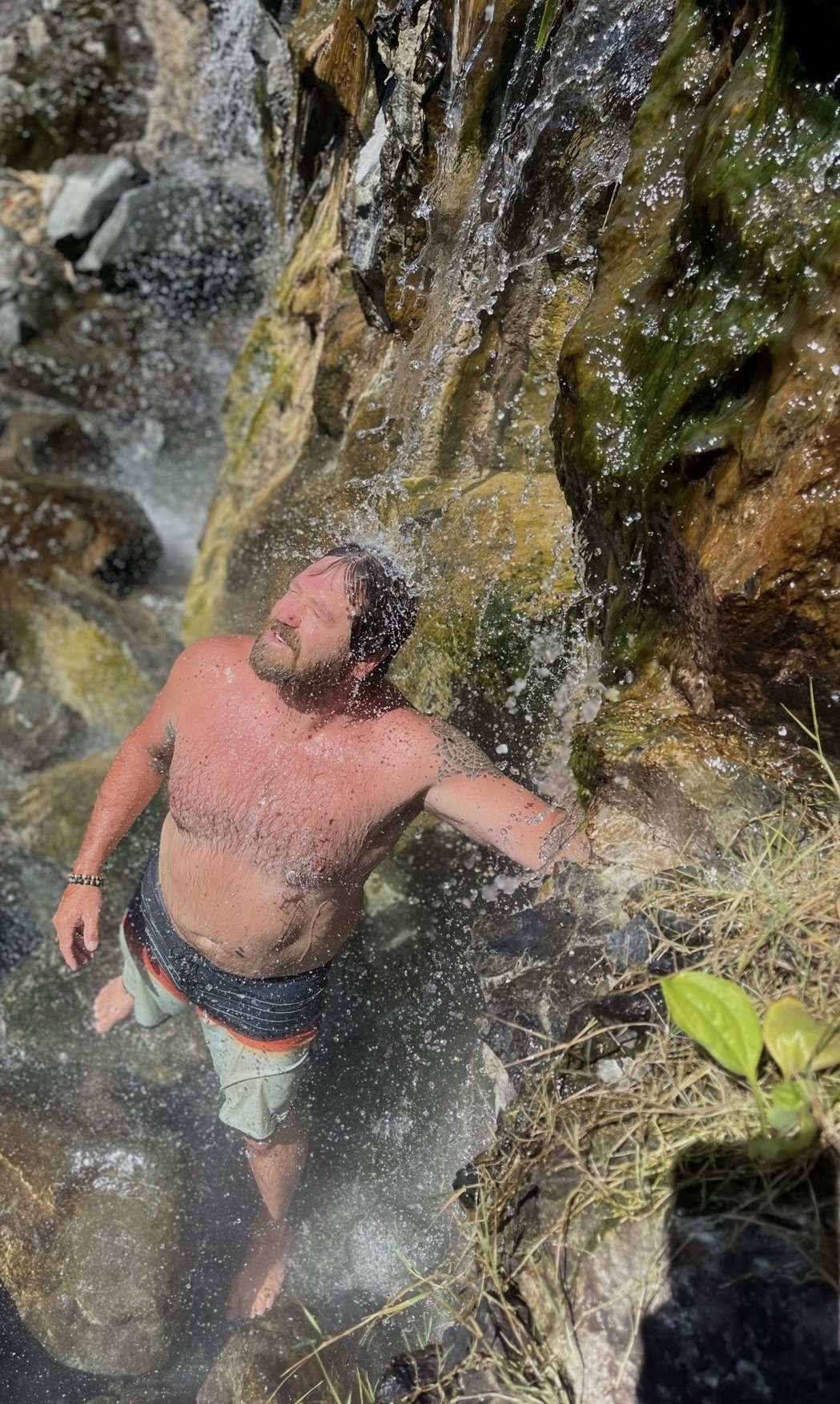 A man standing under a hot spring waterfall with his head tipped back