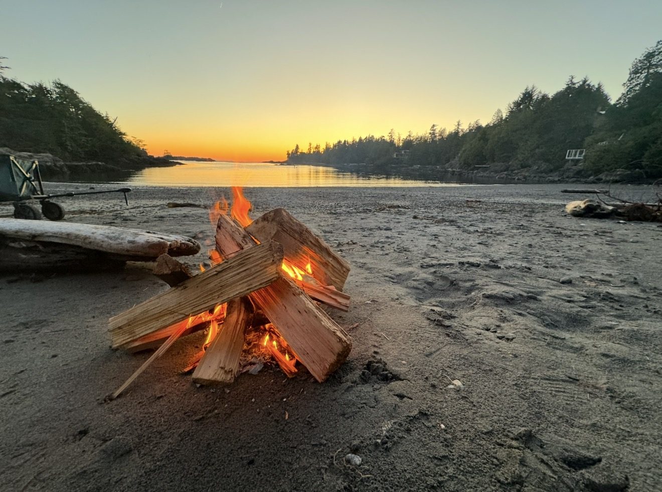 A driftwood-lined cove at sunset with a bonfire burning on the sand