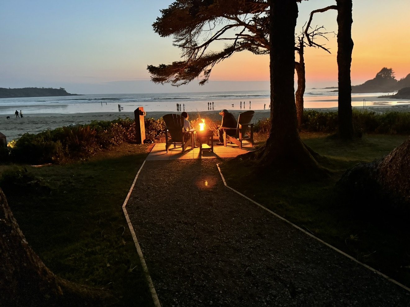 Two people by a fire pit on a Tofino beach at sunset